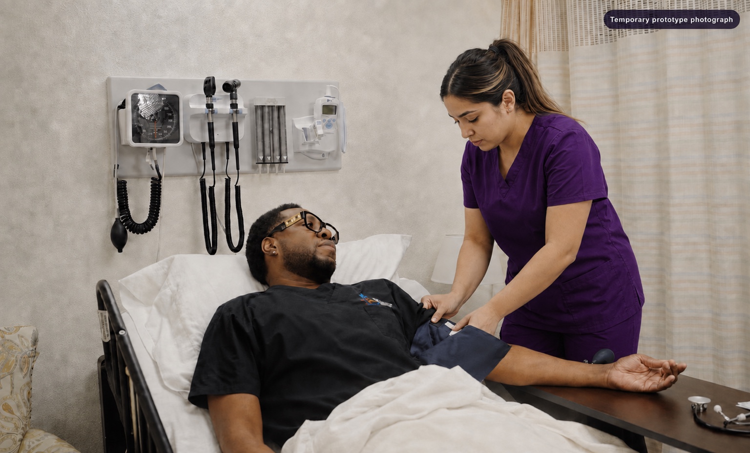 Adult CNA student in purple scrubs practicing a blood-pressure check in a training laboratory